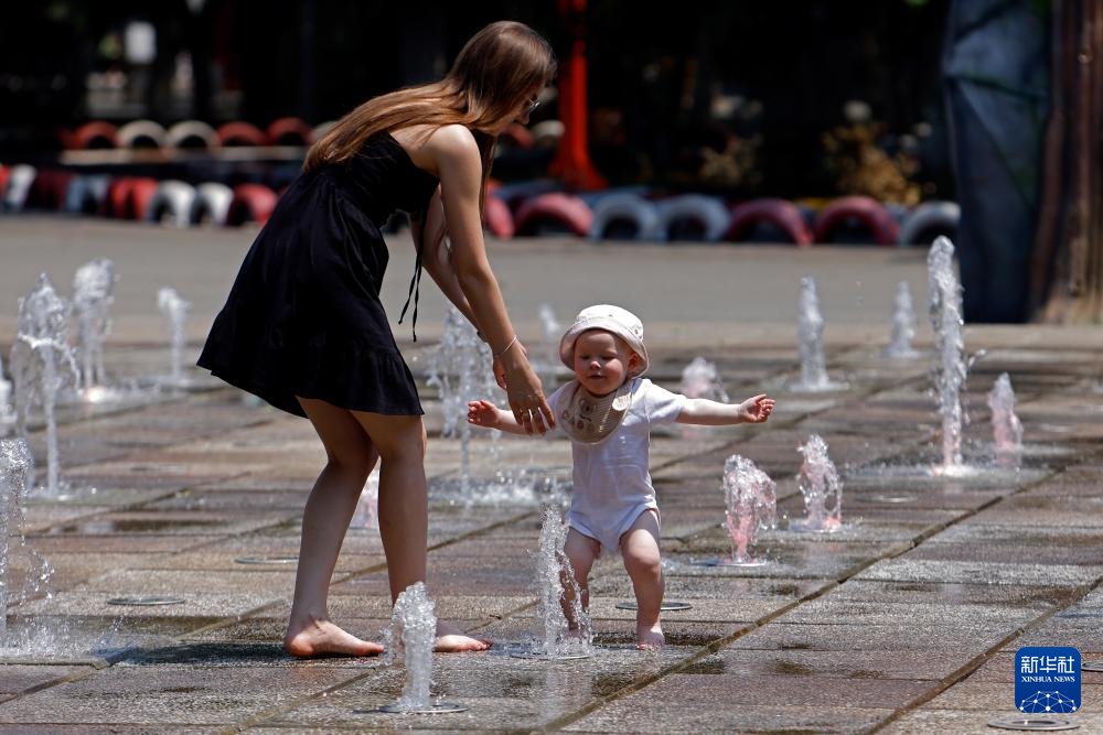 7月8日，在罗马尼亚首都布加勒斯特，一名女子带着孩子在喷泉中纳凉。新华社发（克里斯泰尔摄）