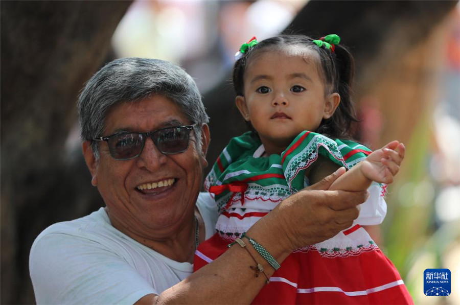 9月16日，在墨西哥瓦哈卡州的瓦哈卡市中心，一名小女孩身着国旗颜色的传统民族服装，在家人带领下参加独立日庆祝活动。新华社记者 李梦馨 摄