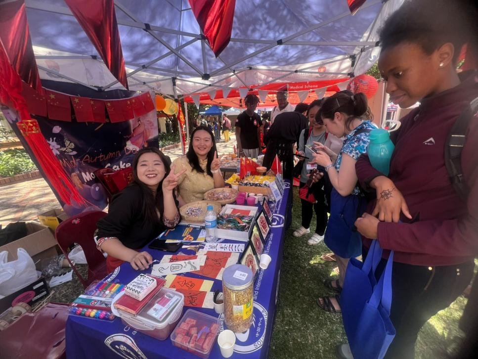 南非中国文化中心孔子课堂严阳媚和周欣钰老师在展台前。南非中国文化中心孔子课堂供图