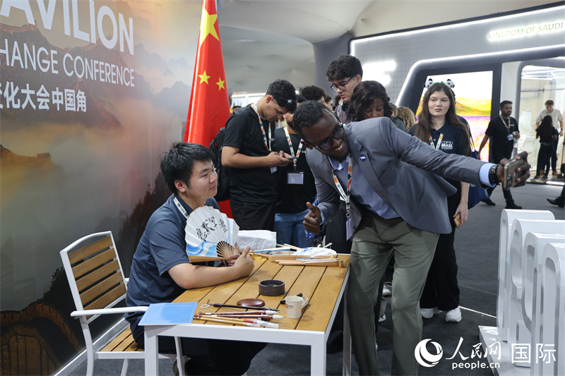 “中国角”外围,参观者与在折扇上进行书法创作的工作人员合影。人民网记者 时元皓摄