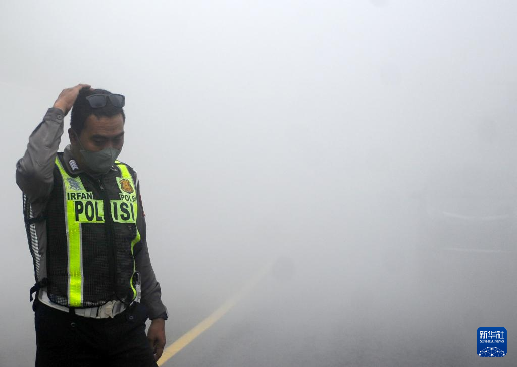 11月21日，在印度尼西亚东爪哇省，一名警察冒着火山灰执勤。新华社发（萨赫兰·库尔尼亚万摄）
