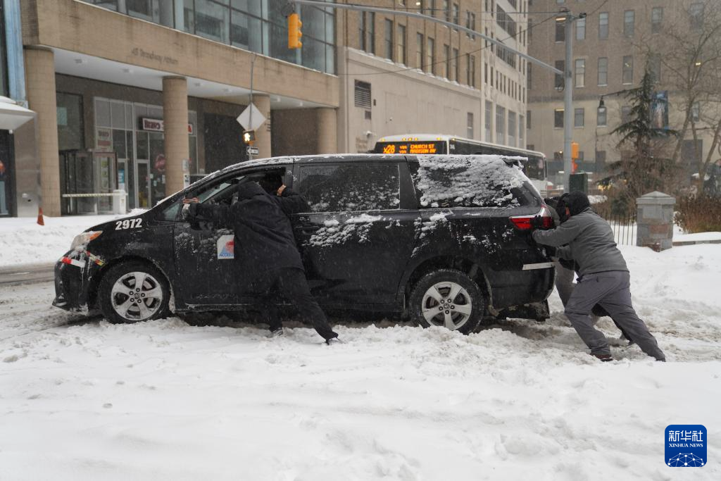 1月25日，在美国纽约，人们推动陷在雪中的汽车。新华社记者 张凤国 摄