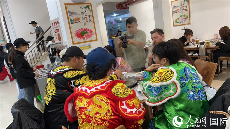 广东汕头,人民网外专柯明可与汕头青年英歌队成员围坐品尝牛肉火锅。人民网 王潇平摄