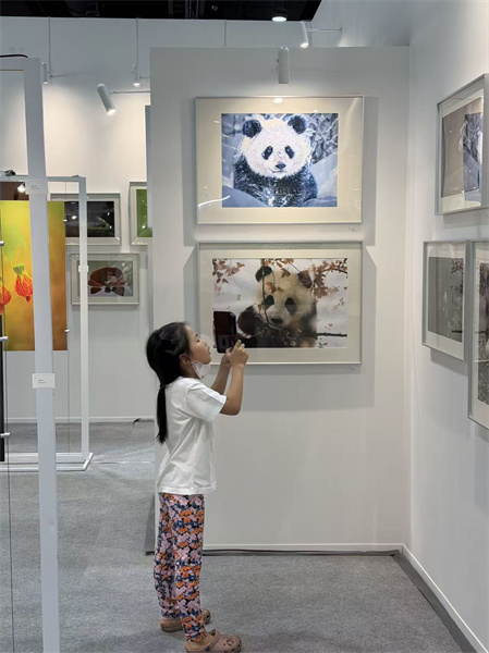 一名泰国小女孩在“绿动中国：熊猫、草木与微距生灵的生态叙事”展览现场拍摄熊猫照片。 中国出版代表团供图