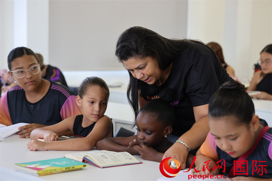 4月2日是国际儿童图书日，巴西里约热内卢北部的曼吉尼奥斯社区芭蕾舞学校开展了一场别具特色的阅读活动，其中中文阅读成为一大亮点。图为老师俯身耐心指导孩子阅读，让缕缕书香浸润童心。人民网实习生 侯天泽摄