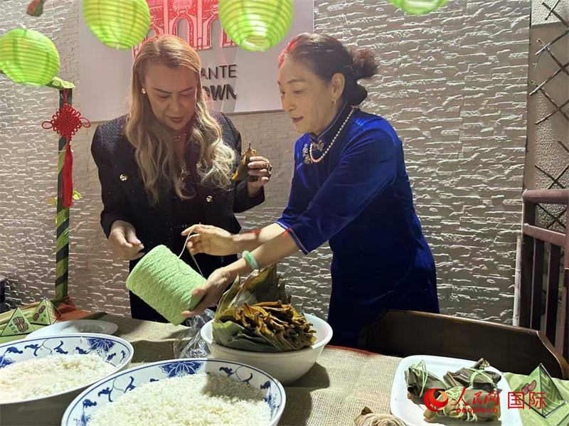 在活动现场，巴西里约热内卢州议会副议长蒂娅·茹（左）在巴西华人联谊会副会长何双莲的指导下，饶有兴致地体验包粽子。 人民网记者 陈一鸣摄