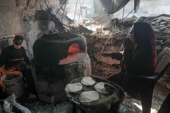 12月15日,在加沙地带中部城市代尔拜拉赫,巴勒斯坦人在被毁坏的房屋中烤制大饼。新华社发(里泽克·阿卜杜勒贾瓦德摄)