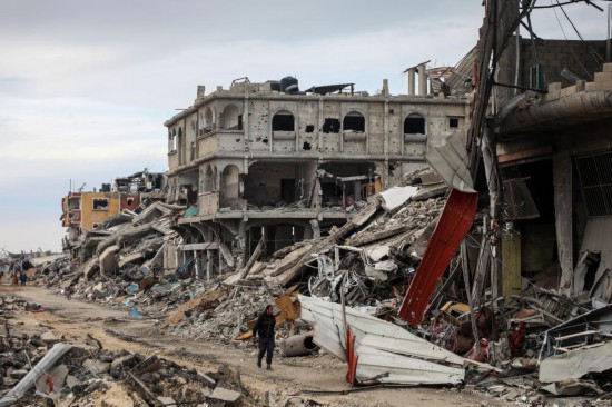 2月9日,在加沙地带内察里姆走廊附近,巴勒斯坦人经过建筑废墟。新华社发(里泽克·阿卜杜勒贾瓦德摄)