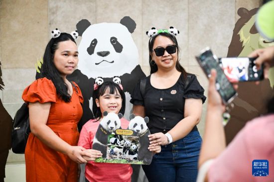 5月17日，在马来西亚吉隆坡的国家动物园，人们在大熊猫馆内举着大熊猫“兴兴”和“靓靓”的牌子合影。新华社记者 程一恒 摄