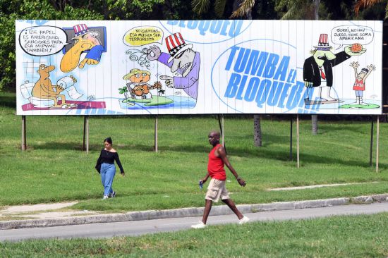 11月5日,在古巴首都哈瓦那,行人从谴责美国对古巴封锁的宣传牌前走过。宣传牌的蓝色大字写着“推翻封锁”,漫画讽刺美国对古巴封锁的荒谬性。 新华社发(华金·埃尔南德斯摄)