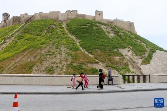 2026年4月16日，人们走过叙利亚阿勒颇城堡。作为阿勒颇古城的一部分，它于1986年被联合国教科文组织列入世界遗产名录。阿勒颇古城位于叙利亚西北部阿勒颇盆地，建城历史可追溯至公元前2000年。古城在近年的战争与地震中遭受严重破坏，城堡墙体、西塔及多处历史建筑受损。2013年，阿勒颇古城被联合国教科文组织列入濒危世界遗产名录。新华社发